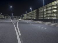 an empty street that has two white lines on it at night in a big industrial area