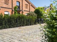 a brick path leads up to the brick facade of an old building with a fence surrounding