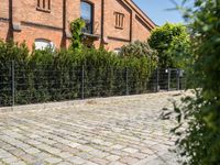 a brick path leads up to the brick facade of an old building with a fence surrounding