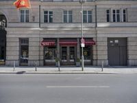 the building has a vietnamese flag hanging from the sidewalk outside of it to protect from the sun