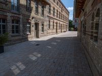 an empty bricked sidewalk between two tall buildings with trees on the side of them