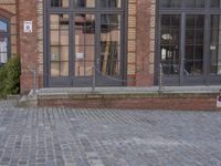 a brick building with a fire hydrant outside of it on a brick sidewalk next to a building that has several large windows