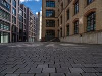 a brick courtyard has steps leading up to it, and a blue umbrella is on the ground