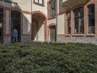 a building with hedges surrounding it in front of a person entering the door from the outside