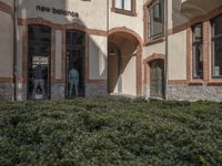 a building with hedges surrounding it in front of a person entering the door from the outside