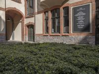 a building with hedges surrounding it in front of a person entering the door from the outside