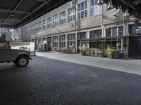 a military vehicle parked inside of a building near a street with brick flooring and potted planters in front of it