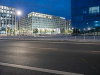 two glass and steel buildings at night near a street with street lights on it and one building with multiple floors