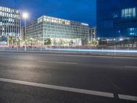 two glass and steel buildings at night near a street with street lights on it and one building with multiple floors