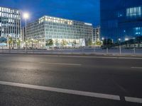 two glass and steel buildings at night near a street with street lights on it and one building with multiple floors