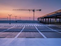 a empty parking lot with construction cranes and traffic lights lit up at sunset from an outdoor area