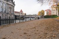 an alley lined with leaves leading to buildings and bridge over water next to it in the autumn