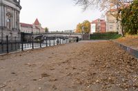 an alley lined with leaves leading to buildings and bridge over water next to it in the autumn