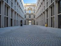 an empty brick courtyard area with two stone columns and two arched windows in the background