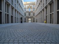 an empty brick courtyard area with two stone columns and two arched windows in the background