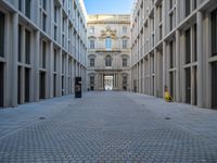 an empty brick courtyard area with two stone columns and two arched windows in the background