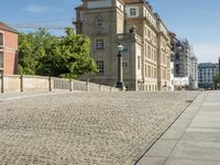 a cobblestone street in front of a large, beige building with windows and a clock tower