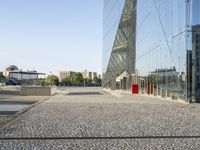 a long walkway is in front of the building's reflection and surrounding its very large windows