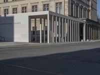 the large white building is next to an empty street of tall pillars and concrete columns