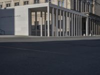 the large white building is next to an empty street of tall pillars and concrete columns