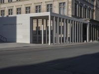 the large white building is next to an empty street of tall pillars and concrete columns