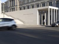 the large, empty sidewalk with multiple columns in front of the building with two signs