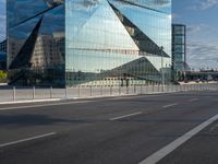 the tall glass building is reflected in the mirror's walls of the building by the street