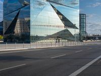 the tall glass building is reflected in the mirror's walls of the building by the street