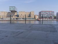 a skateboarder stands in an empty parking lot with buildings in the background of this photo