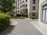 a brick road between two buildings and bushes in front of it and a blue sky with some clouds