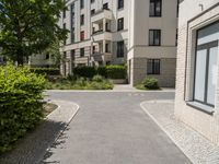 a brick road between two buildings and bushes in front of it and a blue sky with some clouds