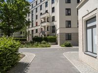 a brick road between two buildings and bushes in front of it and a blue sky with some clouds