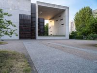 a building with concrete and glass, an entrance in the background and a bench with a wooden seat sitting in front