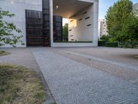 a building with concrete and glass, an entrance in the background and a bench with a wooden seat sitting in front