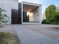 a building with concrete and glass, an entrance in the background and a bench with a wooden seat sitting in front