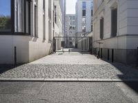 the shadow of a man stands in the narrow walkway between two white buildings on one side and a light pink building on the other