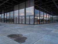 an empty building with large panes of glass reflecting in the puddles of concrete