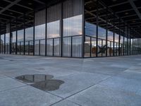 an empty building with large panes of glass reflecting in the puddles of concrete