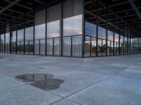 an empty building with large panes of glass reflecting in the puddles of concrete