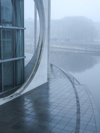 a building with a circle window overlooking some water in the fog while onlookers are talking