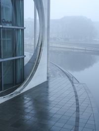 a building with a circle window overlooking some water in the fog while onlookers are talking