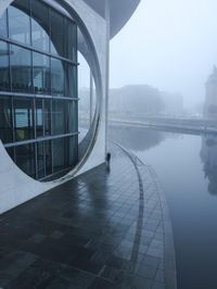 a building with a circle window overlooking some water in the fog while onlookers are talking
