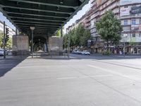 cars and pedestrians pass under a train track in an old part of the city, with trees lining either side