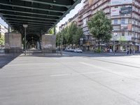 cars and pedestrians pass under a train track in an old part of the city, with trees lining either side