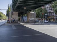 cars and pedestrians pass under a train track in an old part of the city, with trees lining either side