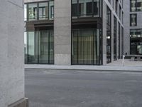 a woman in red top standing on the corner of an empty street next to tall buildings