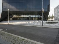 large glass building with benches near a street corner on a sunny day from outside the area