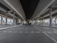 an empty street with streetlights and cars passing underneath it, with overpasses