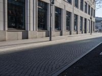 a sidewalk with a bench and brick sidewalk and building with a sky background and reflection on water