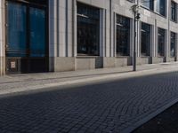a sidewalk with a bench and brick sidewalk and building with a sky background and reflection on water